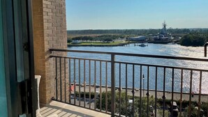 A balcony with a view of a river, a dock with a boat, and a distant building.