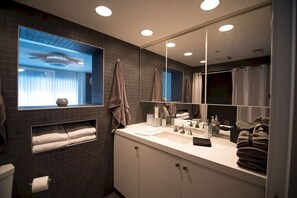 Une salle de bain moderne avec un grand miroir, une fenêtre avec des rideaux, un lavabo avec des articles de toilette et un porte-serviettes.
