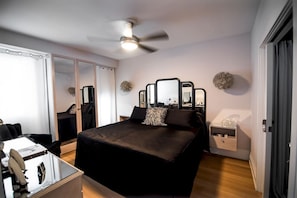 Une chambre à coucher moderne, équipée d’un lit, d’un ventilateur de plafond, d’une table de chevet et d’une armoire.
