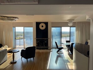 Een moderne woonkamer met een open haard, een eethoek en grote ramen met uitzicht op zee.