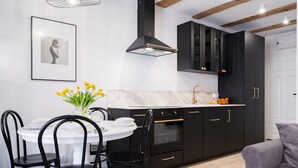 A modern kitchen with black cabinets, a white countertop, and a black stove. There is a dining table with black chairs and a vase of yellow flowers. - Miodowa Faktoria 7 (Torun)