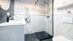 A modern bathroom with a glass-enclosed shower, a white marble sink, and a black floor. - Miodowa Faktoria 7 (Torun)