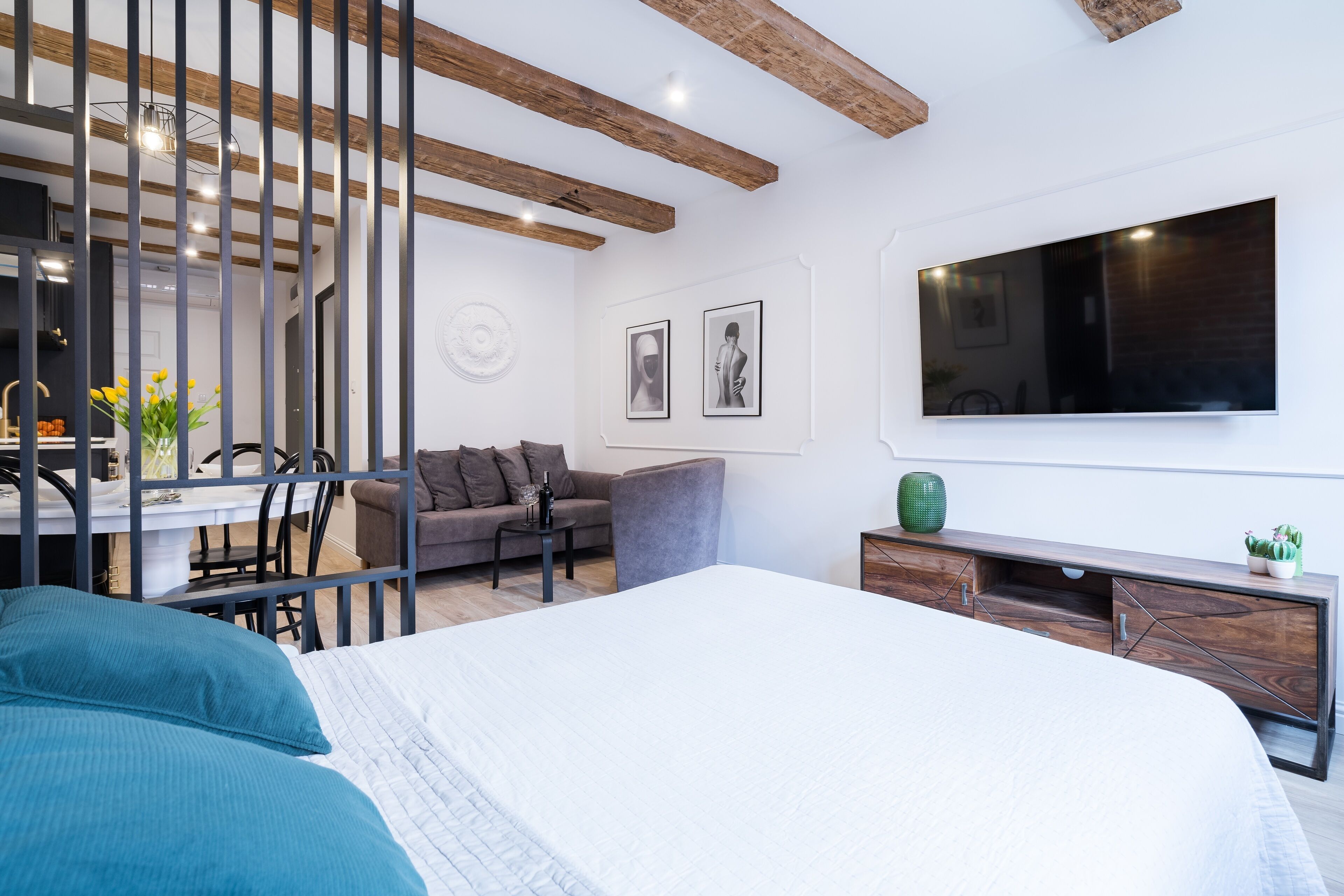 A modern bedroom with a large bed, a desk, a sofa, and a TV mounted on the wall.