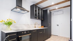 A modern kitchen with dark cabinetry, a marble countertop, and a built-in oven. - Miodowa Faktoria 7 (Torun)