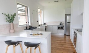 Une cuisine moderne avec des meubles blancs, un îlot central doté de tabourets, un évier et un four à micro-ondes.
