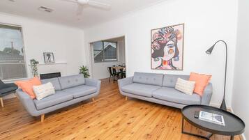 Ein modernes Wohnzimmer mit zwei grauen Sofas, Holzboden, Deckenventilator, einem Gemälde und einem Tisch mit einer Zeitschrift.
