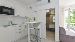 A modern kitchen with white cabinets, a built-in microwave, and a bar area with stools. - Seagull Apartments & Studios (Novalja)
