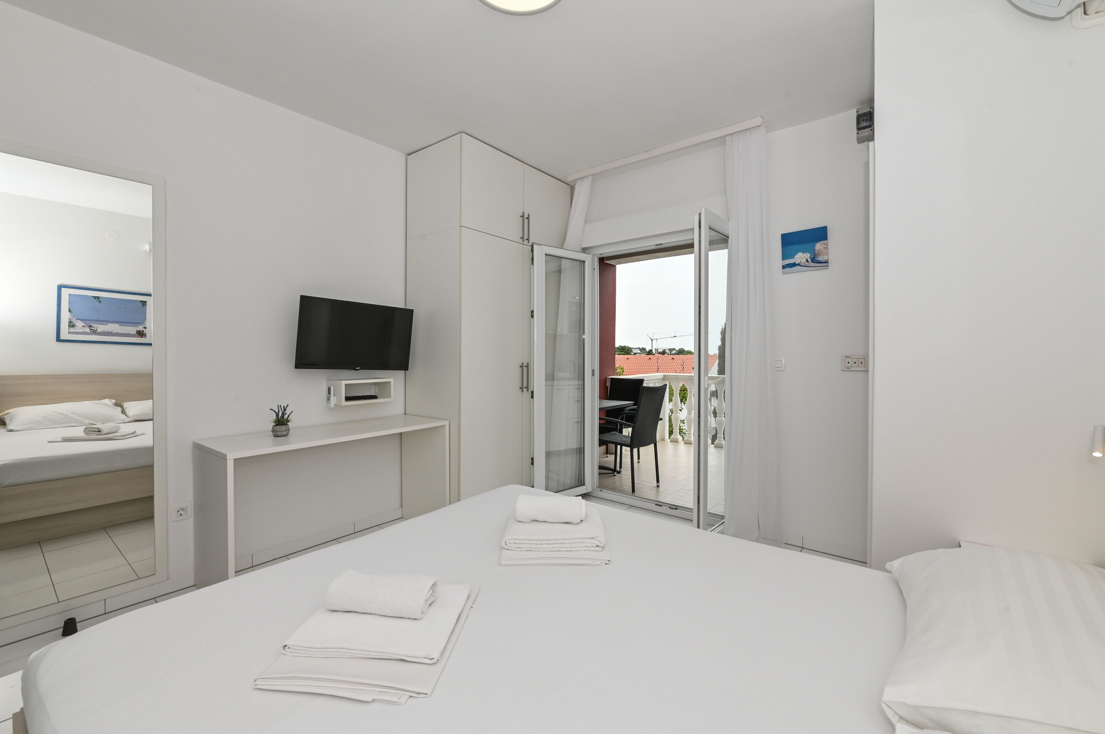 A modern hotel room with a large bed, a TV, a small desk, and a sliding glass door leading to an outdoor area.
