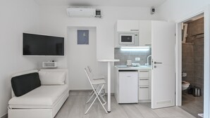 A compact living space with a sofa, a small table, a microwave, and a TV mounted on the wall. - Seagull Apartments & Studios (Novalja)