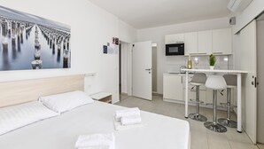 A modern hotel room with a large bed, a painting of a waterfront, a kitchenette, and a small dining area. - Seagull Apartments & Studios (Novalja)