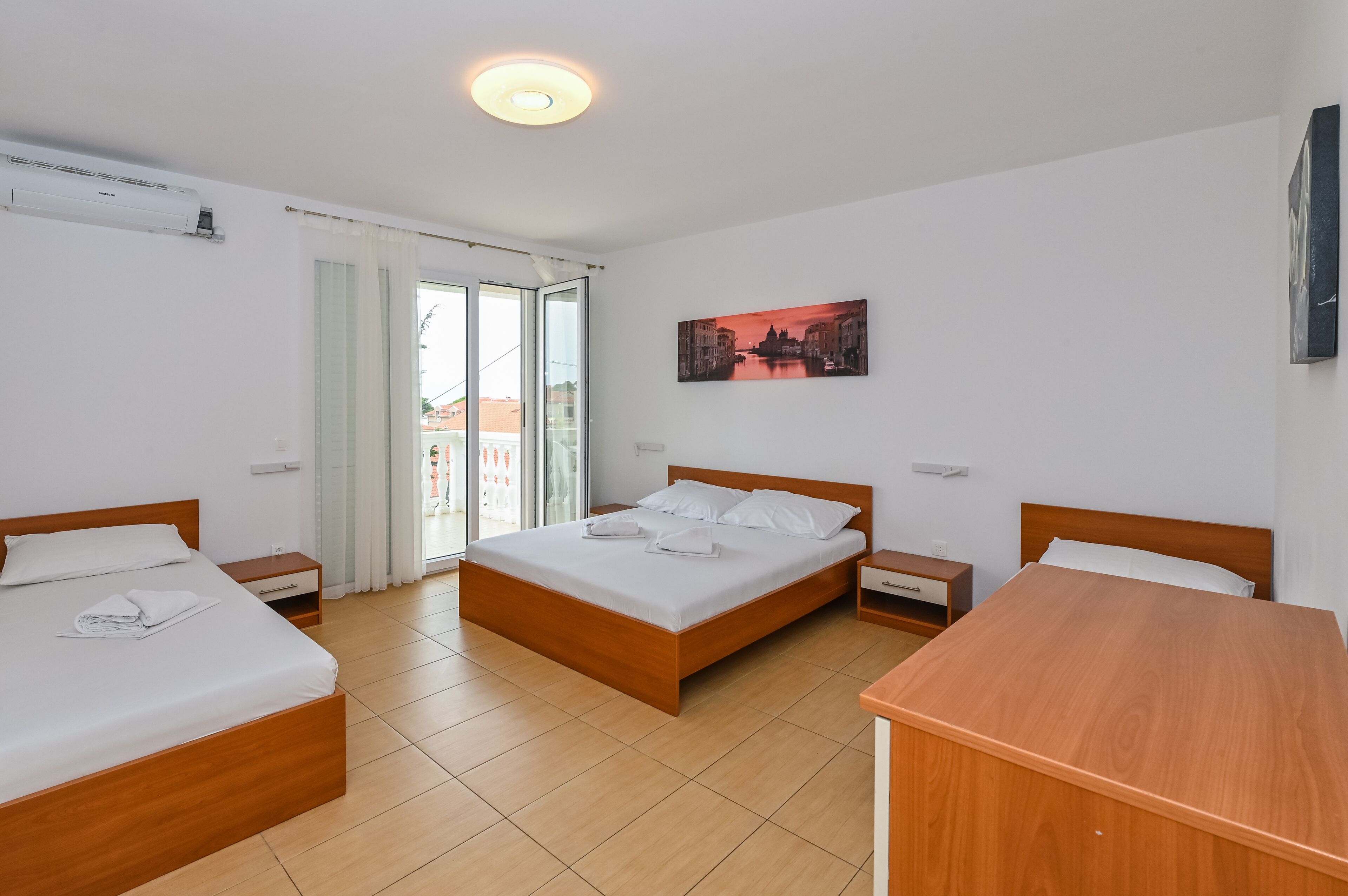 Een hotelkamer met twee enkele bedden, een houten bureau en een groot raam met gordijnen.