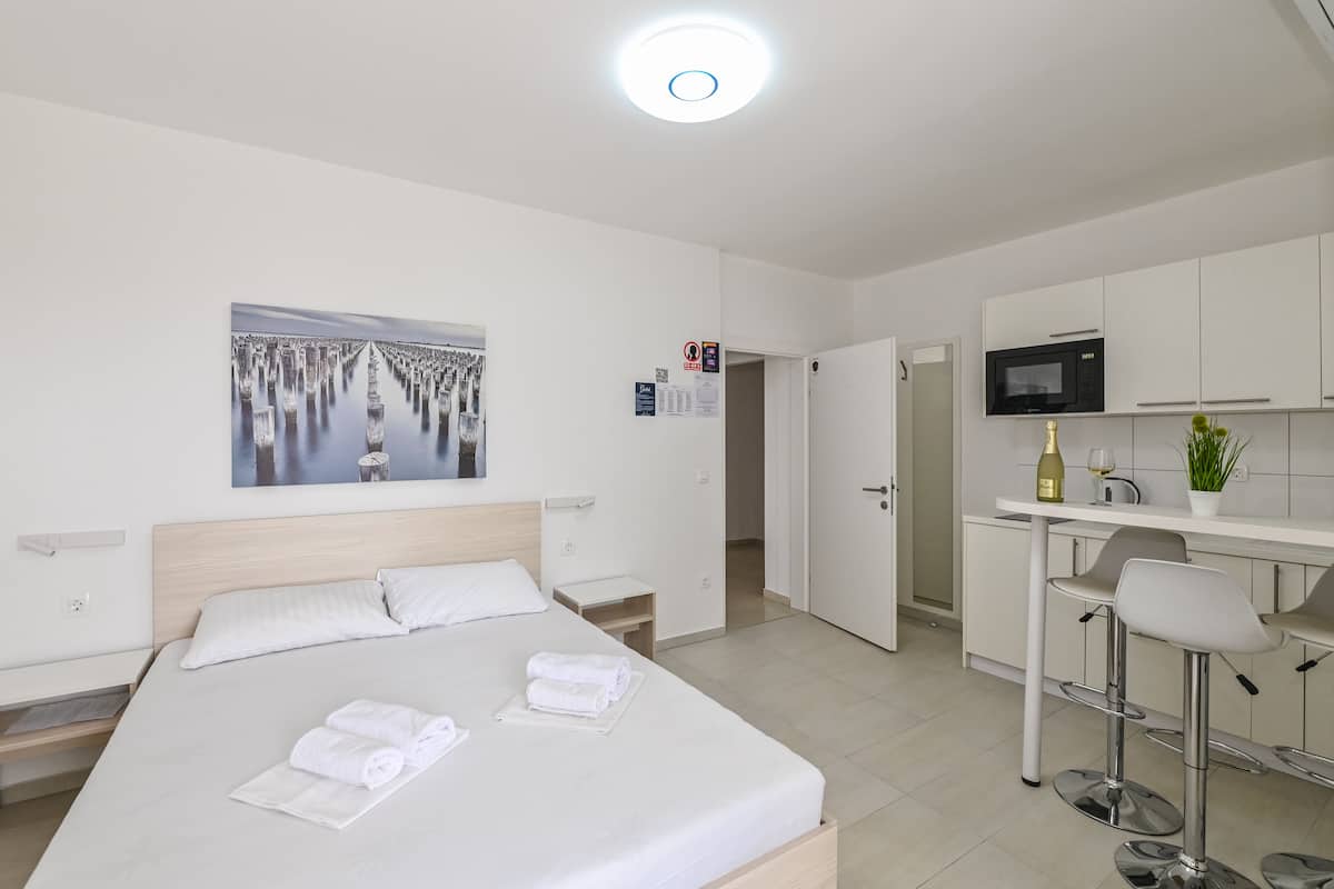 Moderni hotellihuone, jossa on sänky, taulu, keittotila mikroaaltouunilla sekä baarituoli.