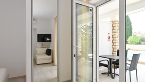 A modern living room with a sofa, a flat-screen TV, and a sliding glass door leading to an outdoor patio with a table and chairs. - Seagull Apartments & Studios (Novalja)