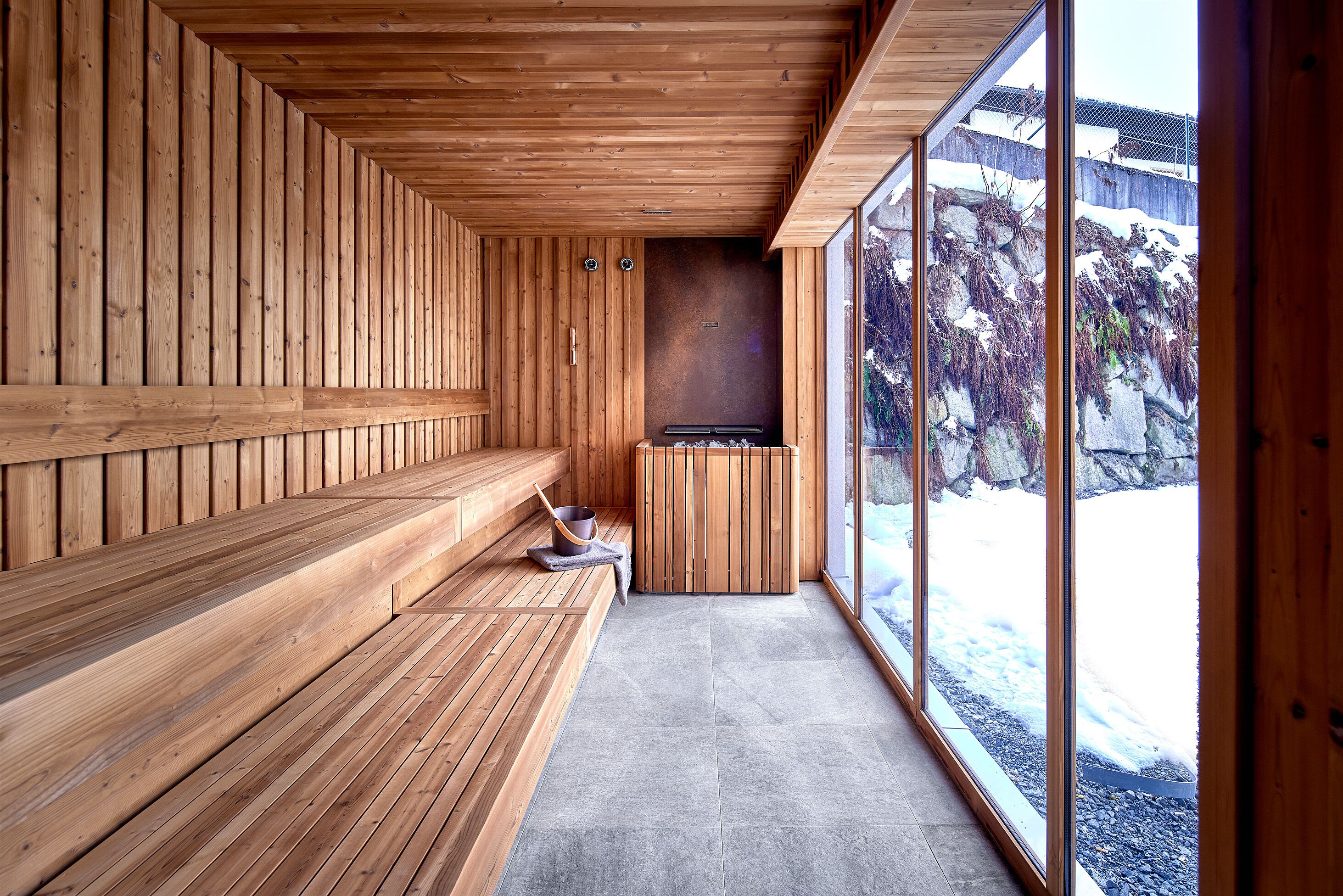 Un sauna en bois, avec des bancs et un mur en pierre, de grandes fenêtres et une vue sur un paysage enneigé.
