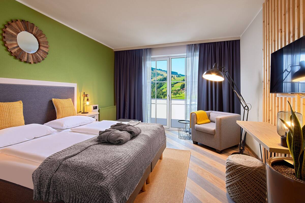 A hotel room with a large bed, a desk, a chair, a TV, and a view of the outdoors.