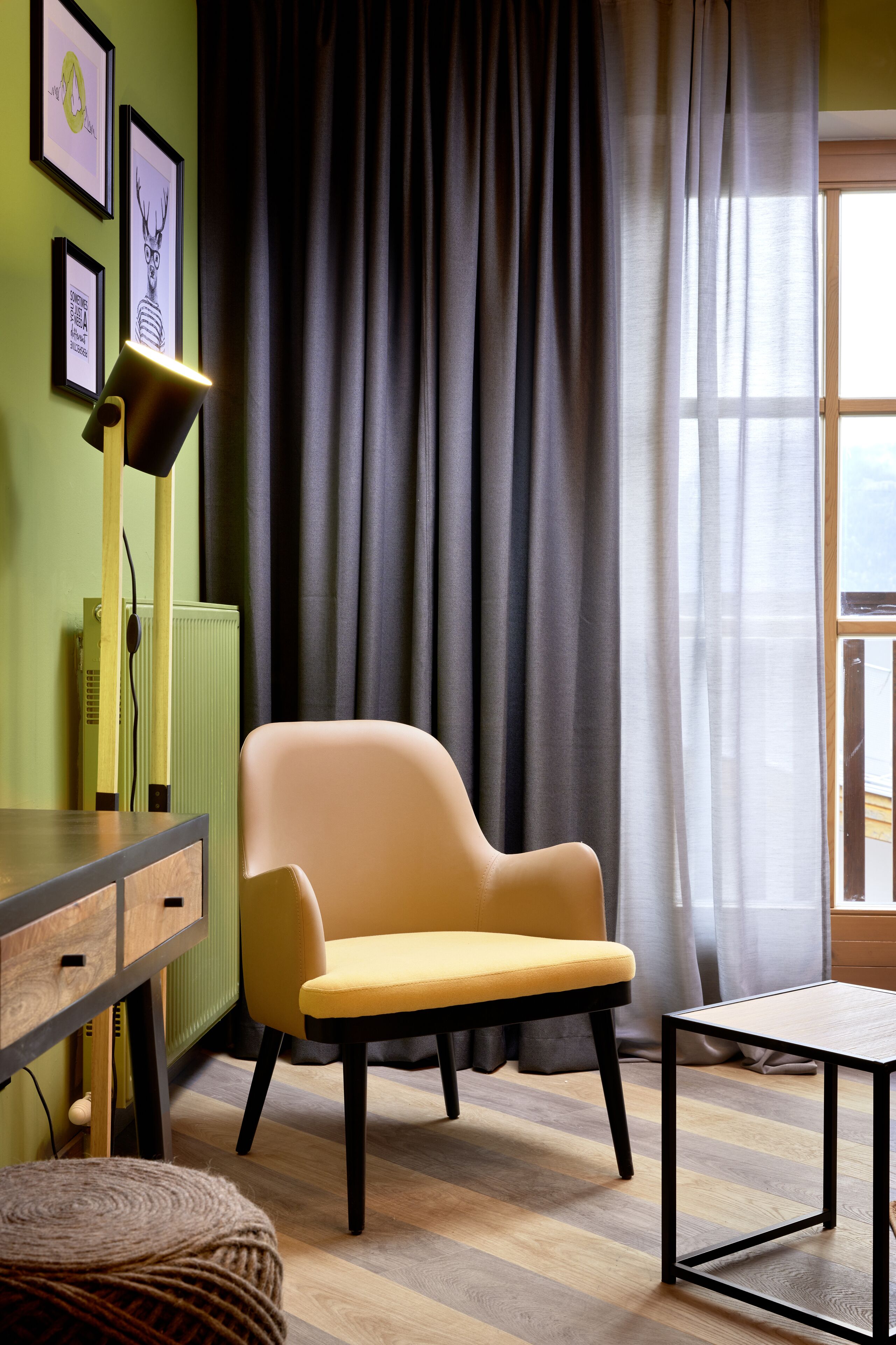 A room with a yellow armchair, a small table, a lamp, and framed pictures on the wall.