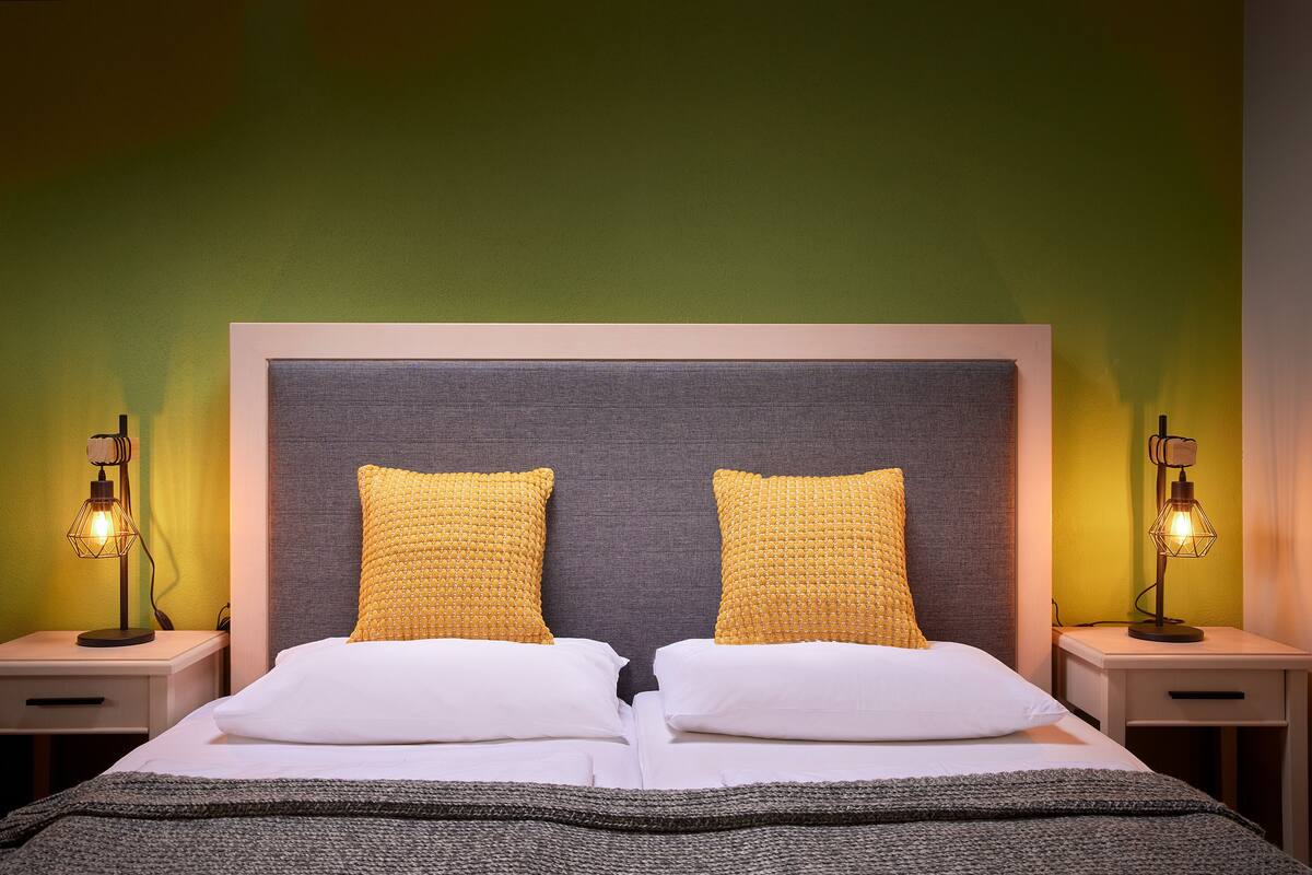 A neatly made bed with two pillows, a grey headboard, and two bedside lamps on nightstands.