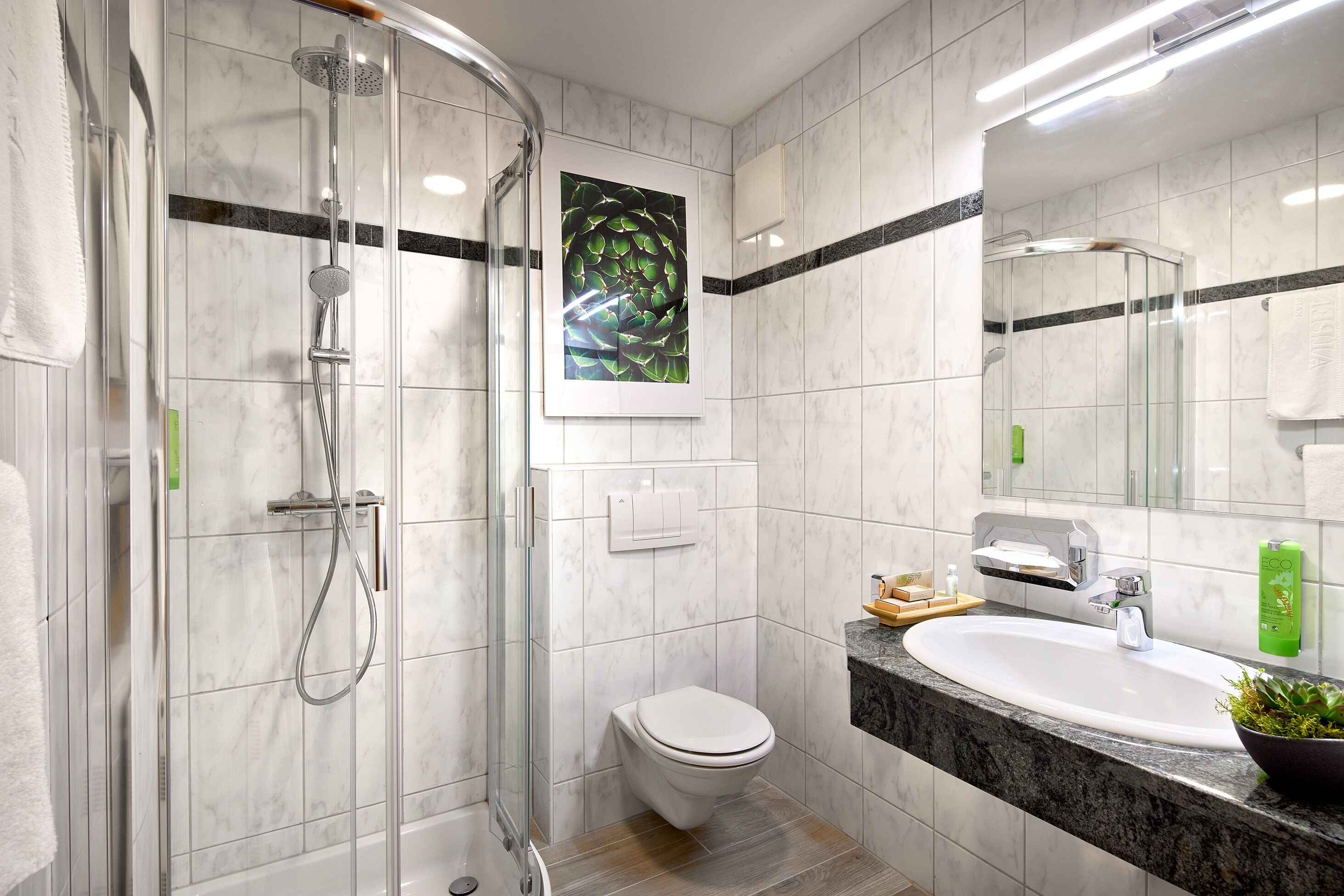 A modern bathroom with a glass-enclosed shower, a white toilet, and a sink with a marble countertop.