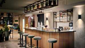 A modern bar area with a wooden bar counter, bar stools, and shelves with bottles and glasses. - ever.grün Kaprun (Kaprun)
