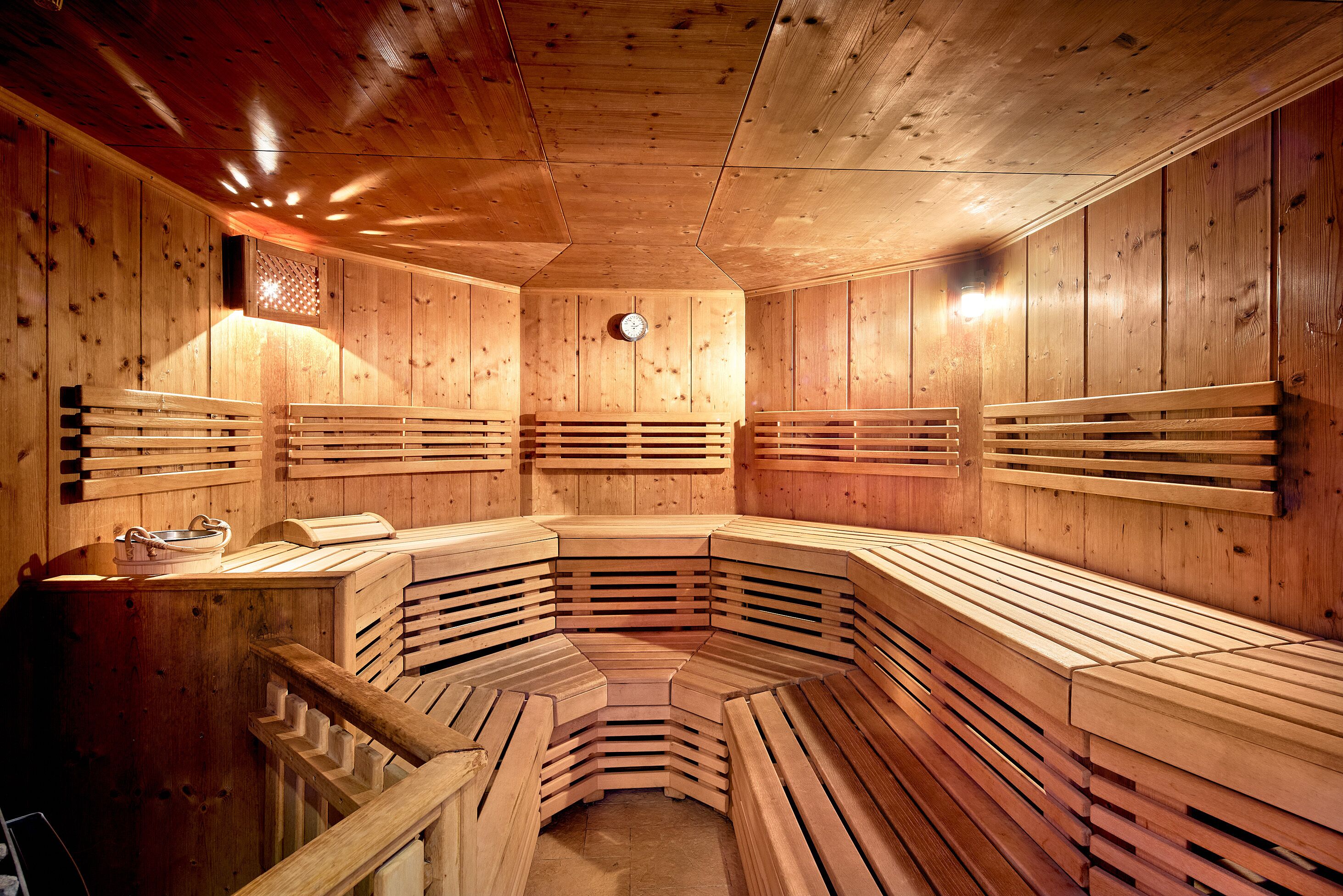 A sauna with wooden benches arranged in a semi-circular pattern, a clock on the wall, and a small table with a towel and a bucket.