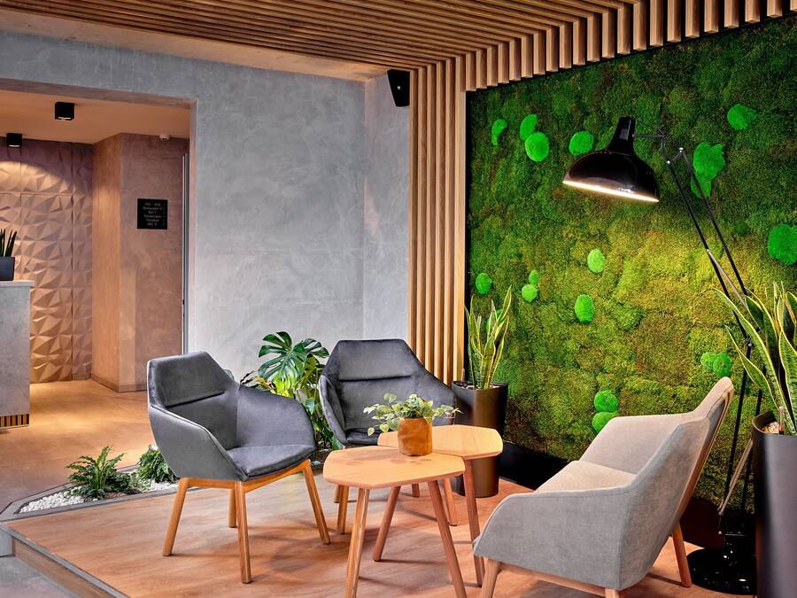Un interior moderno con pared cubierta de musgo verde, sillas tapizadas en gris y una mesa de madera.