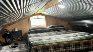 A bedroom with a sloped ceiling, a bed with a plaid bedspread, a wooden floor, a small table with a fan, and a window. - Fox Pen Cabins
Cabin #2
Not friendly for street bikes…
Pet-Friendly (Eminence)