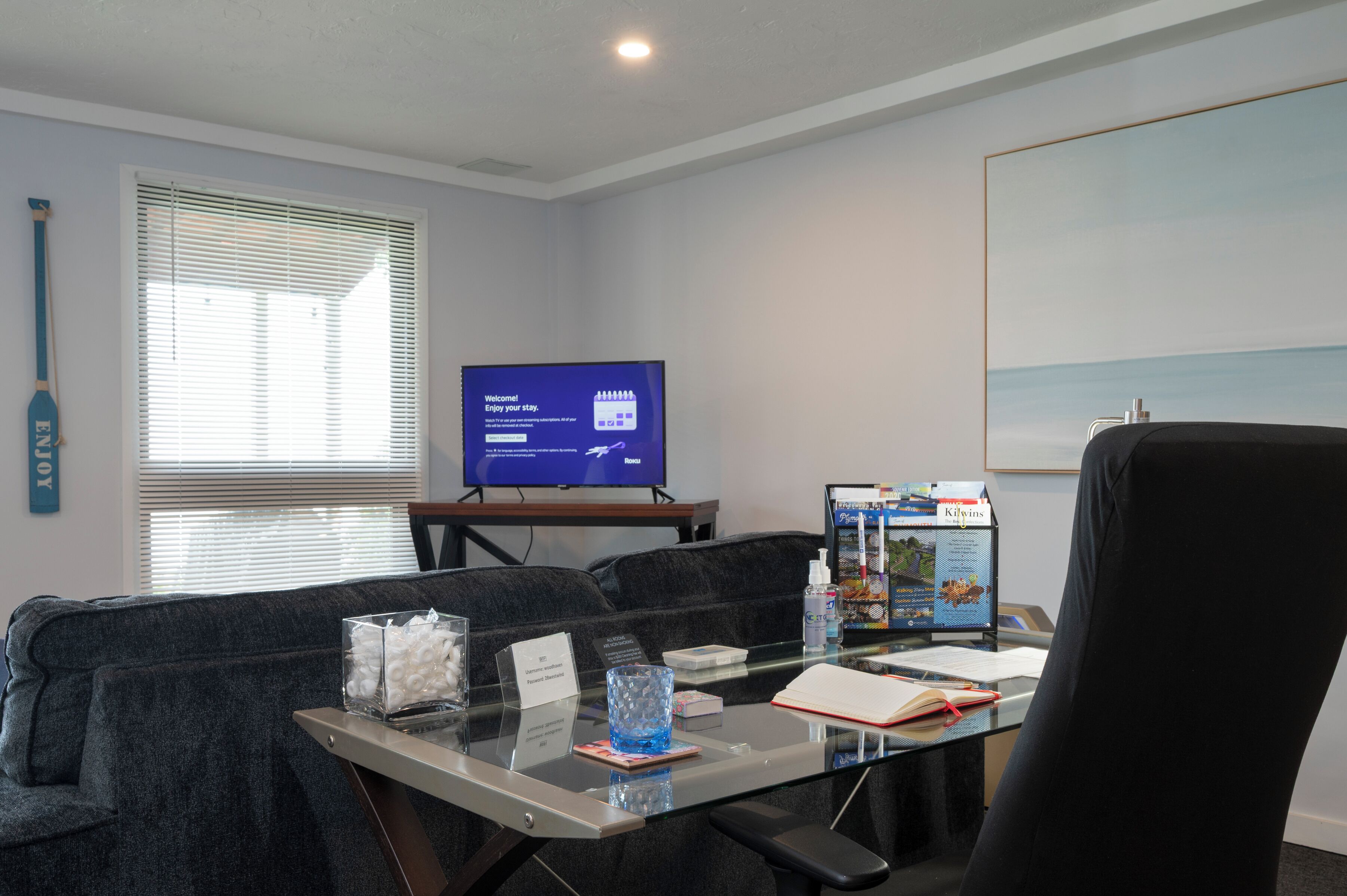 A hotel room with a glass desk, a television displaying a welcome message, a sofa, and a framed picture on the wall.