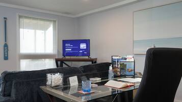 A hotel room with a glass desk, a television displaying a welcome message, a sofa, and a framed picture on the wall.