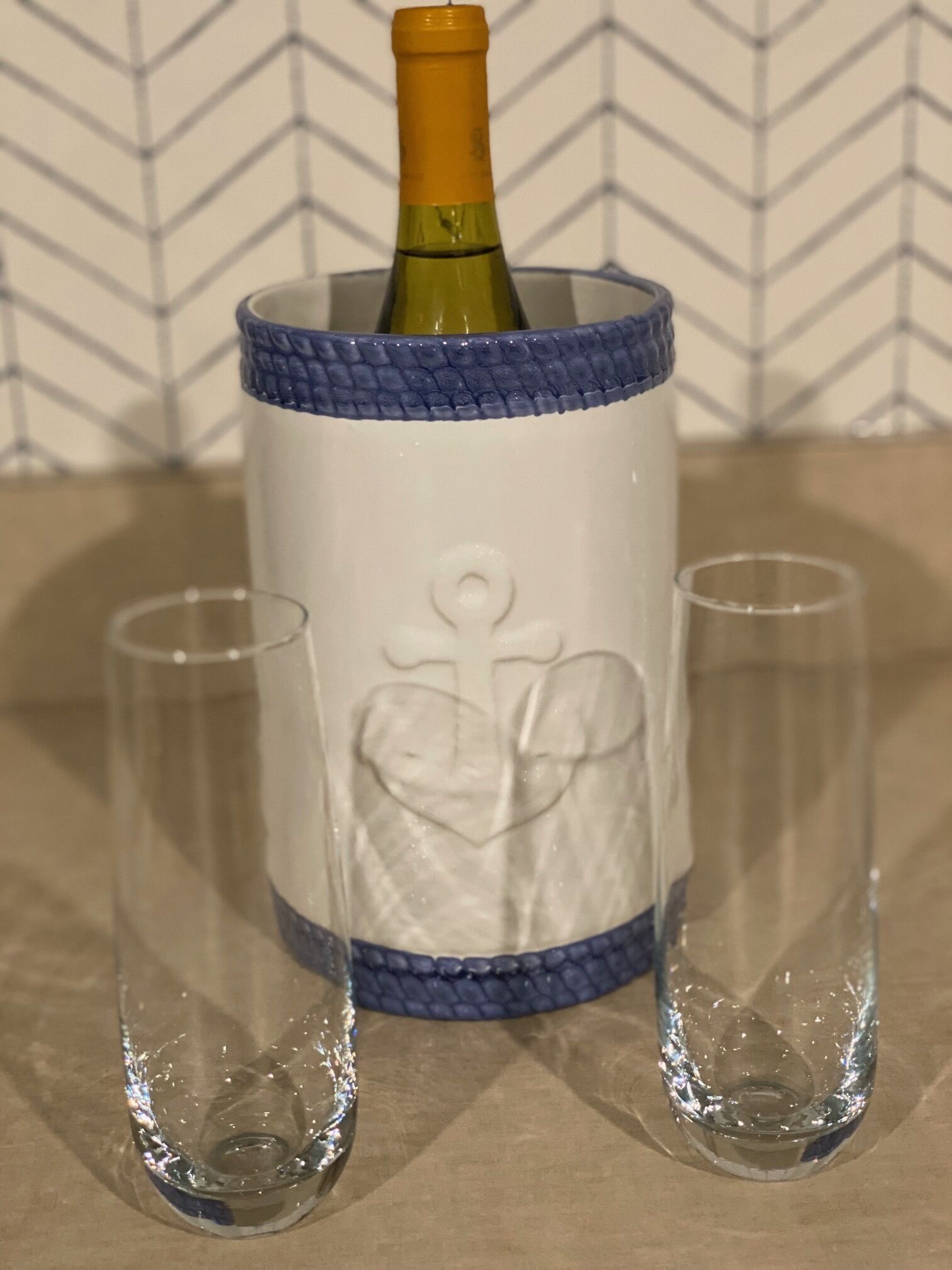 A bottle of champagne in a decorative holder with two glasses beside it.