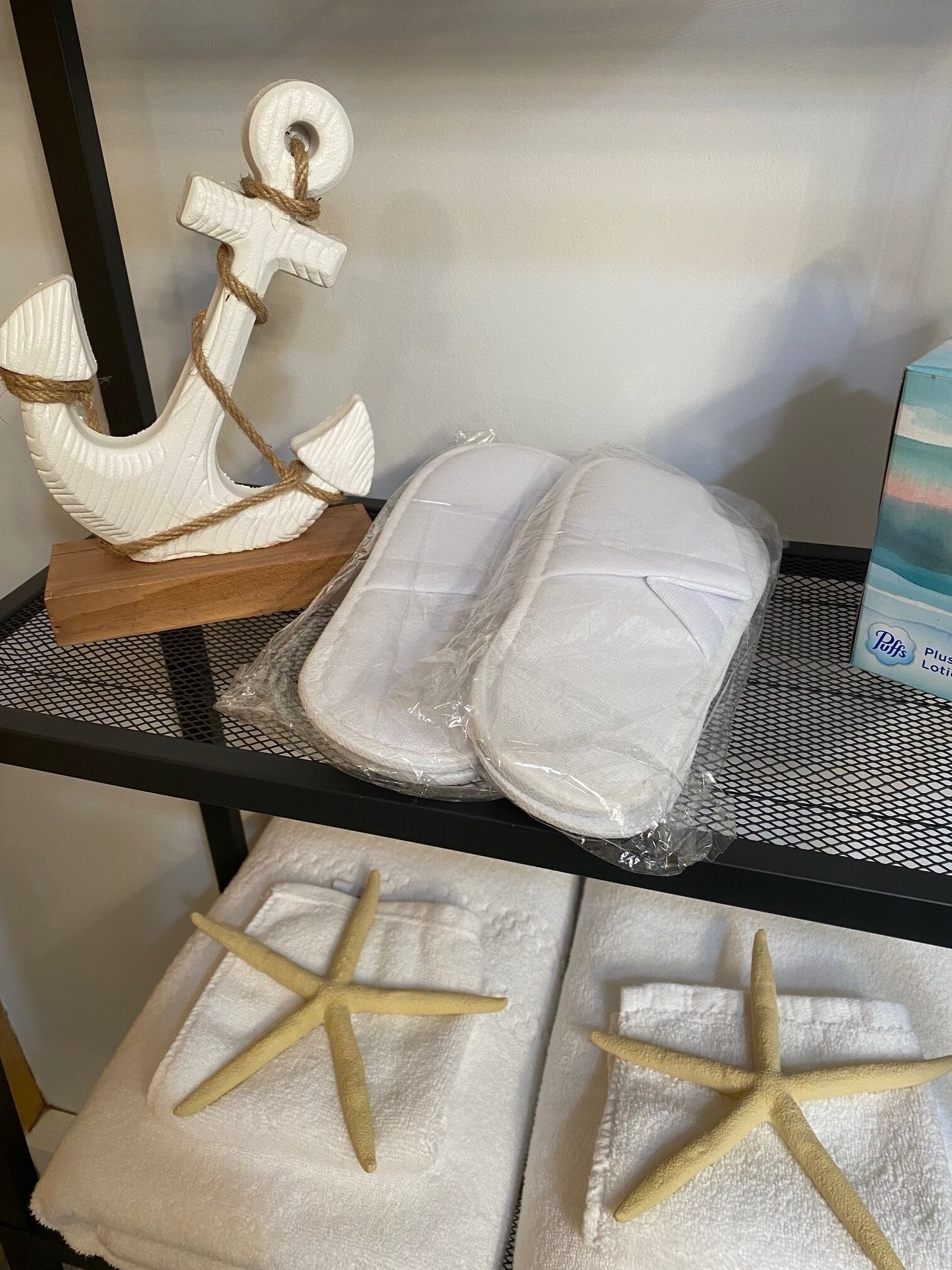 A shelf with a white anchor, two rolled-up towels, and a box of towels.