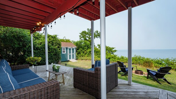 Eine überdachte Terrasse im Freien mit Korbmöbeln, einem kleinen Tisch und Stühlen.