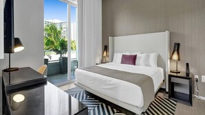 Een moderne hotelkamer met een groot bed, twee bedlampen, een bureau met een lamp, en uitzicht op palmbomen en gebouwen.