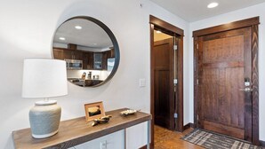 A hallway with a wooden console table, a round mirror, and a dark wooden door.