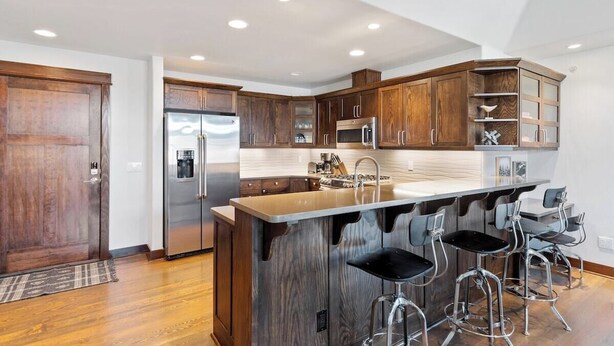 A modern kitchen with wooden cabinets, stainless steel appliances, and a bar area with stools.