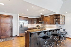 A modern kitchen with wooden cabinets, stainless steel appliances, and a bar area with stools. - Whitefish Condo, just steps from Downtown! (Whitefish)
