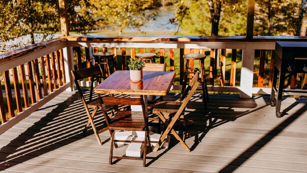 A wooden deck with a table and chairs, overlooking a body of water and trees. - Lost Hill Lake Sunshine Skoolie, The Sunshine Skoolie - Lost Hill Lake (Saint Clair)
