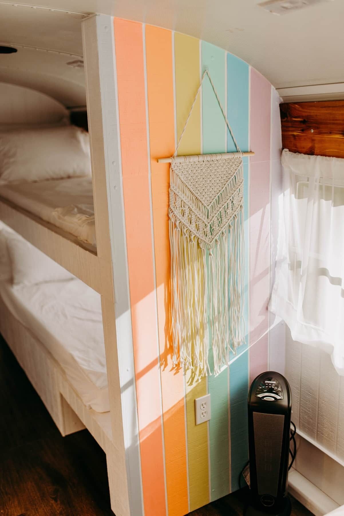 A bunk bed with a colorful striped wall and a macrame wall hanging.