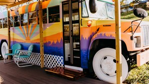A colorful bus with a covered deck and a few chairs. - Lost Hill Lake Sunshine Skoolie, The Sunshine Skoolie - Lost Hill Lake (Saint Clair)
