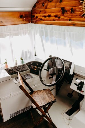 Control room with a steering wheel and wooden chair, perfect for observation or rest.