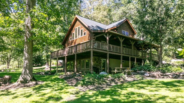 A wooden cabin with a porch, surrounded by trees and a grassy yard. - Eagle Bend Lodge-center of Pine Creek Rail Trail (Brown Township)