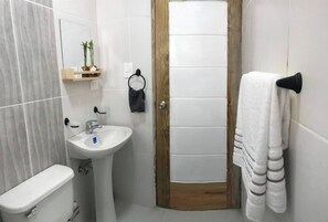 A bathroom with a white sink, toilet, and wooden door. There is a towel rack with a white towel hanging on it.