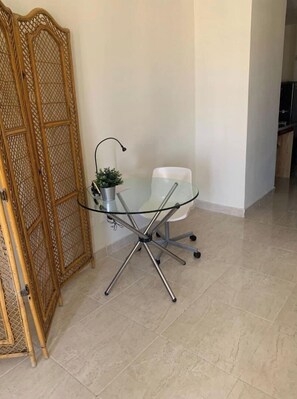 Ein Tisch mit Glasplatte und Metallgestell, ein weißer Stuhl und ein Blumentopf.