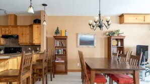 A dining area with wooden furniture, a chandelier, and a bookshelf. - Big White Beauty! Sleeps 10.  Ski in/Ski out Chalet with Private Hot Tub. (Beaverdell)