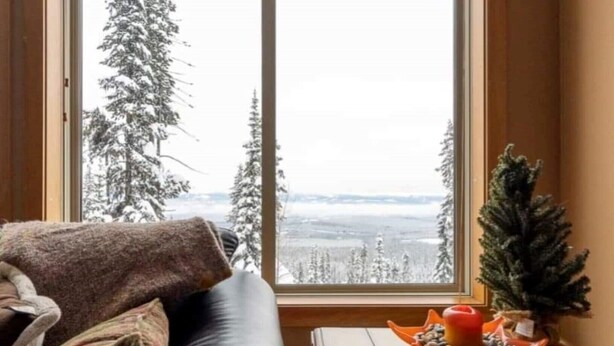 A room with a large window offering a view of snow-covered trees and a distant landscape. - Big White Beauty! Sleeps 10.  Ski in/Ski out Chalet with Private Hot Tub. (Beaverdell)