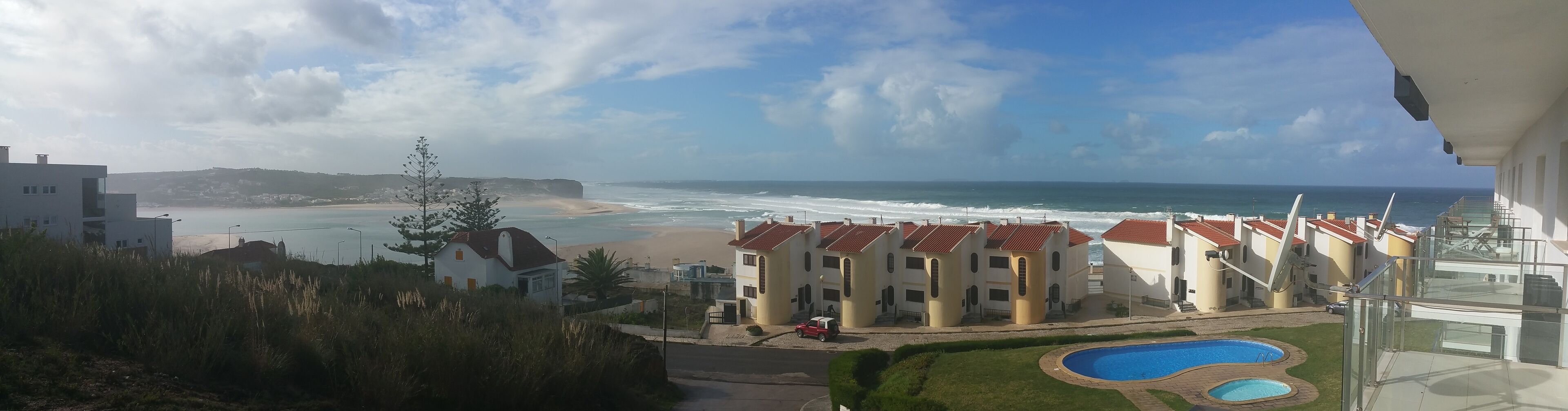 Une vue côtière avec une plage, l’océan et une rangée de maisons aux toits rouges.