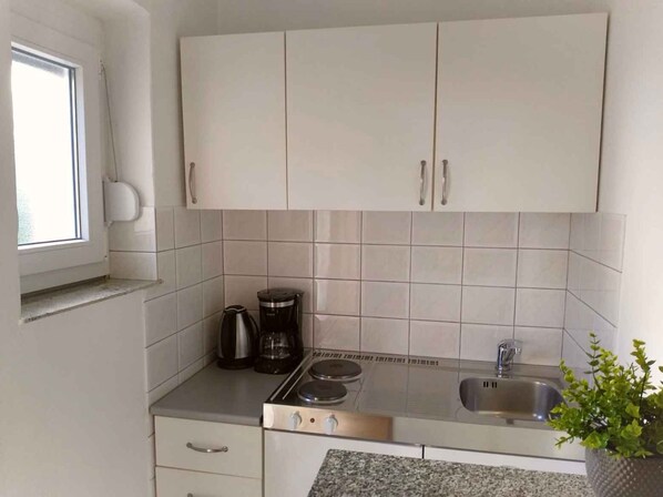 A kitchen with white cabinets, a stove, a sink, and a window.