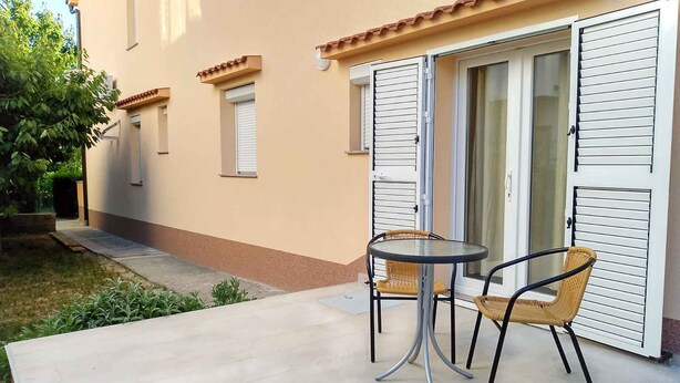 A patio with a table and two chairs, a sliding glass door, and a small garden area. - Studio for 2 people in a quiet part of town (Baška)