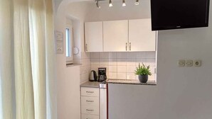 A compact kitchen with white cabinets, a coffee maker, a potted plant, and a flat-screen TV mounted above the counter. - Studio for 2 people in a quiet part of town (Baška)
