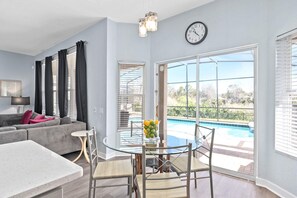 A modern living room with a glass dining table, a sofa, and a view of a swimming pool.