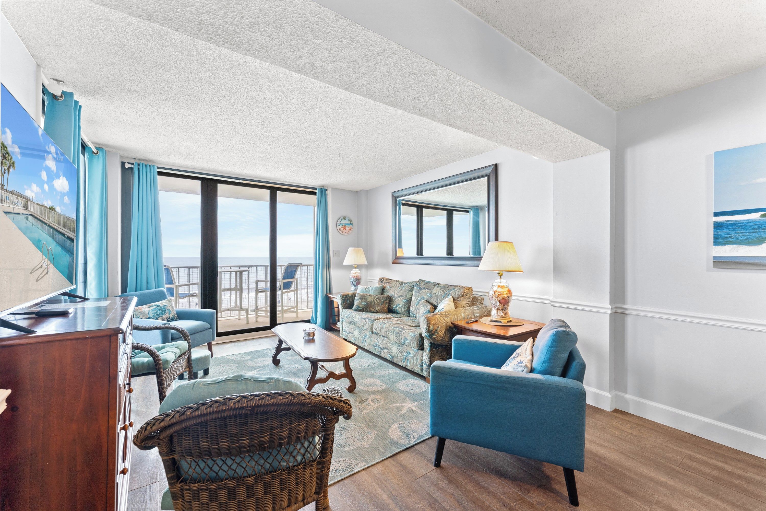 A room with a balcony, a sofa, a chair, a table, and a lamp.